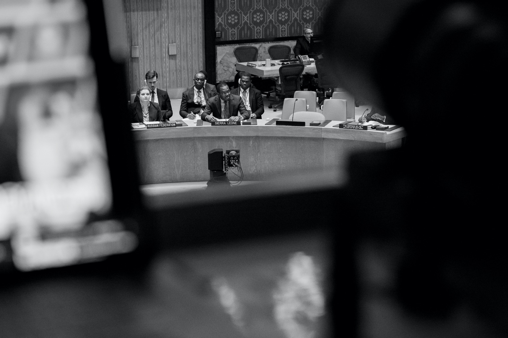 Camera viewfinder in foreground with man attending meeting in focus.