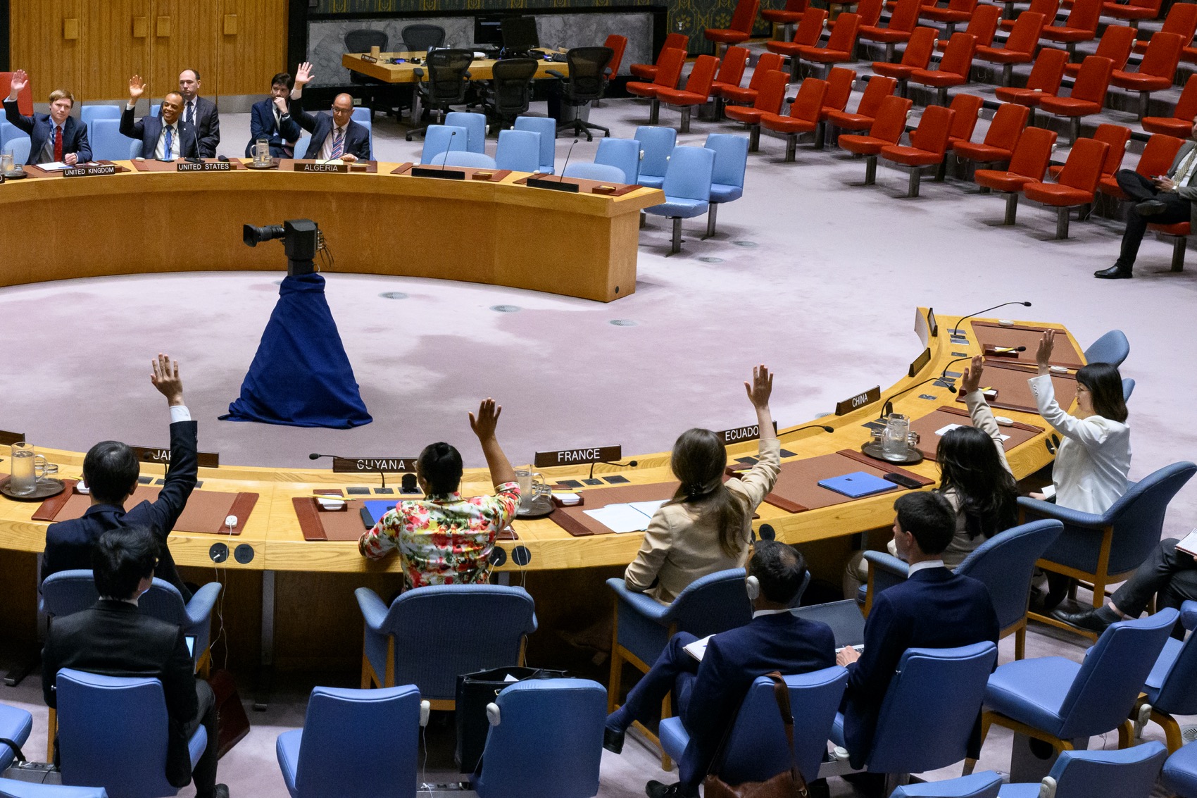 Side view of meeting chambers with some attendees raising hands.