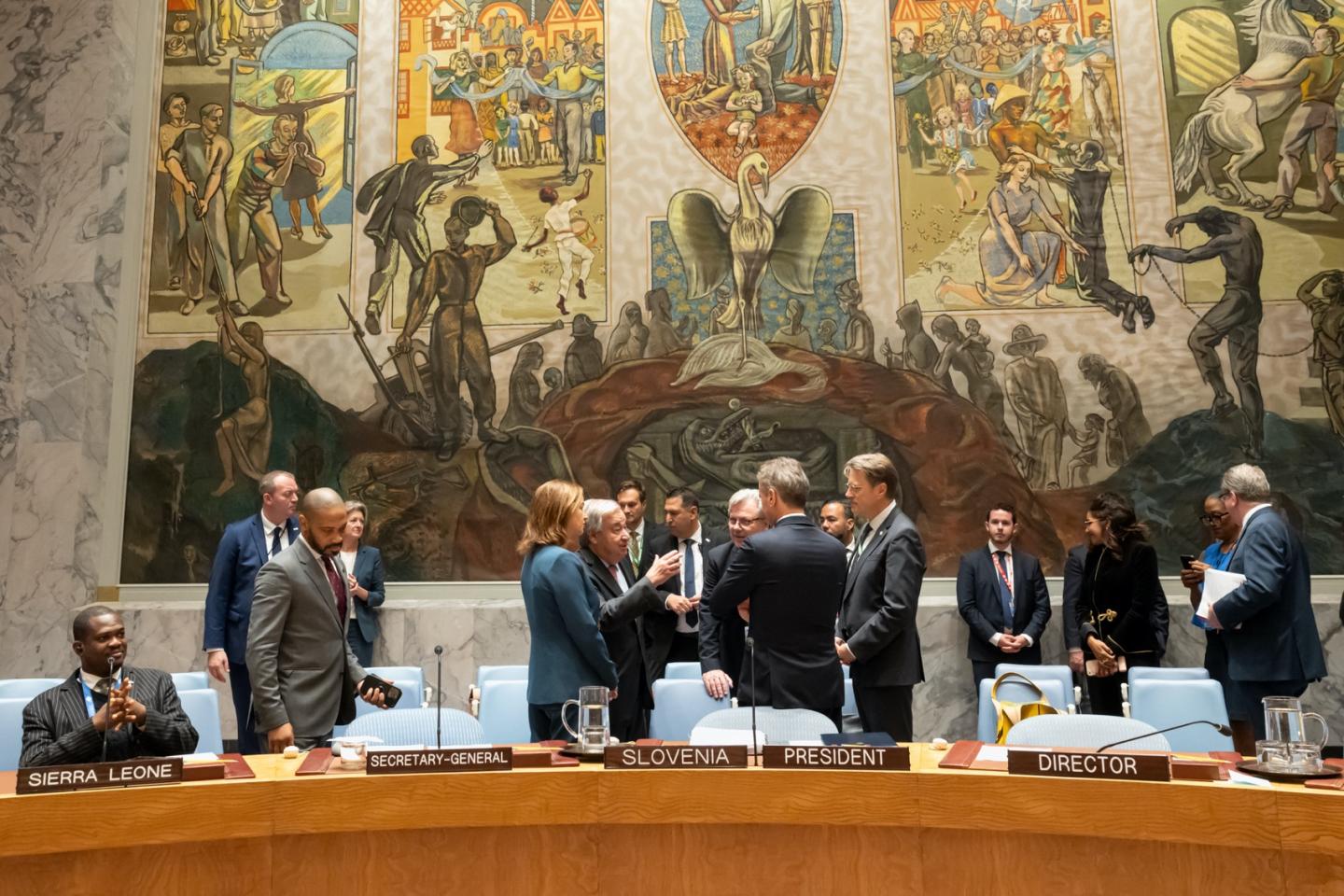 Meeting attendees engaged in discussion beneath large mural.
